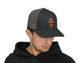 May include: A black trucker hat with a gray mesh back and a curved brim. The hat features an orange, textured cross design on the front. The hat is worn by a person wearing a black hoodie.