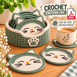 May include: A set of sage green and cream crochet cat-shaped coasters with a matching round storage basket. The coasters feature embroidered whiskers, a small nose, and pointed ears. Text on the image reads CROCHET PATTERN PDF and STEP BY STEP INSTRUCTIONS.
