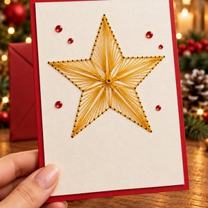 Può includere: Un biglietto d'auguri rettangolare con un pannello frontale color crema caratterizzato da un design a stella realizzato con arte del filo dorato. Il biglietto ha un bordo rosso ed è decorato con piccoli strass rossi rotondi.