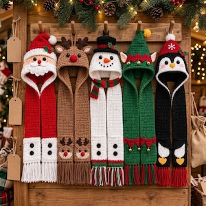 May include: Five crochet hooded scarves featuring holiday characters: a red Santa, a brown reindeer, a white snowman, a green elf, and a black penguin. Each scarf has a character hood, long panels, and fringed ends, displayed hanging on wooden hooks.