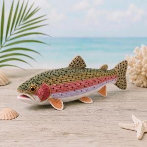 May include: A handcrafted crochet rainbow trout fish toy featuring a textured olive green back with black spots, a pink lateral stripe, and a white underbelly. The fish has orange fins, a detailed gill cover, and a realistic brown eye.