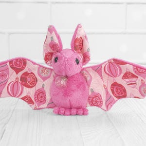 May include: Pink plush bat with fabric wings featuring a pink and white ornament pattern.