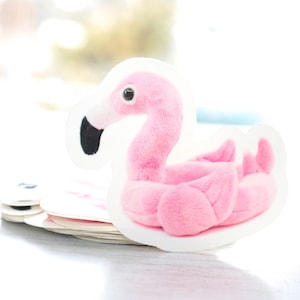 May include: Pink plush flamingo toy shaped like a pool float. The flamingo has a black beak and white eyes.