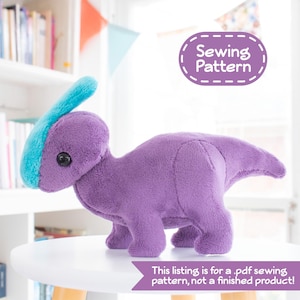 Puede incluir: Un patrón de costura de dinosaurio de peluche morado y azul. El patrón es para un dinosaurio pequeño con una cresta azul en la cabeza. El texto "Sewing Pattern" está en un óvalo blanco con un borde discontinuo.