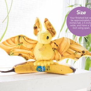 A yellow banana themed bat plush sits on top of a banana. A text overlay describes the size (available in the product description)