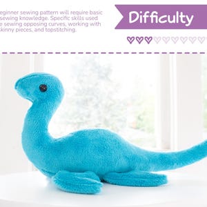 K&ouml;nnte beinhalten: Ein t&uuml;rkisfarbenes Pl&uuml;schtier des Ungeheuers von Loch Ness, mit langem Hals und Schwanz sowie kleinen flossenartigen F&uuml;&szlig;en. Das Spielzeug hat ein schwarzes Knopfauge. Das Bild enth&auml;lt Text mit "Schwierigkeit" und Details zum Schnittmuster.