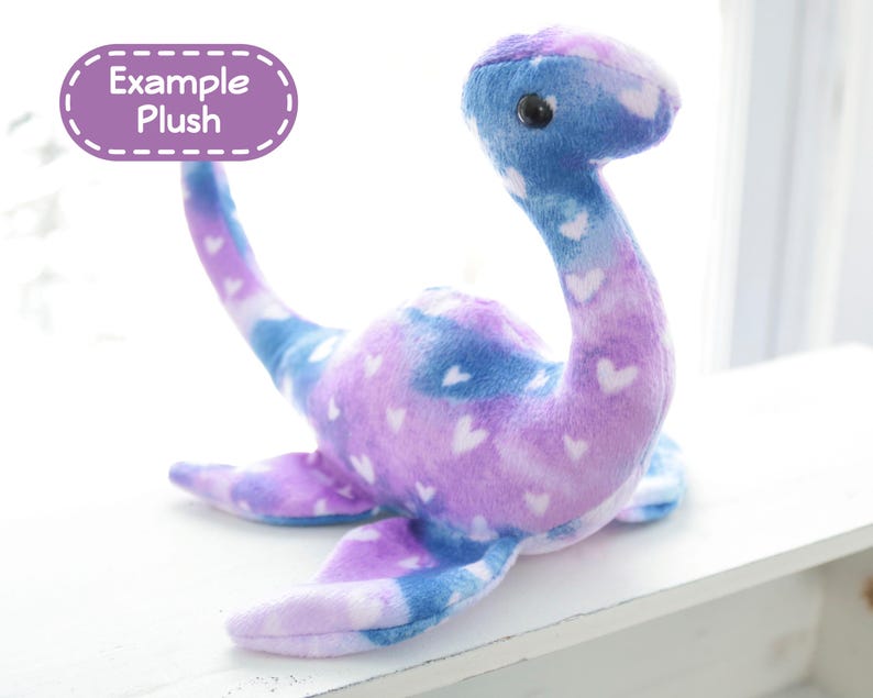 K&ouml;nnte beinhalten: Ein Pl&uuml;schtier in Form eines Seeungeheuers, in Blau, Lila und Wei&szlig; mit Herzmustern. Das Spielzeug hat einen langen Hals, Flossen und ein kleines, rundes Auge. Der Text "Example Plush" befindet sich in einem lila Oval.
