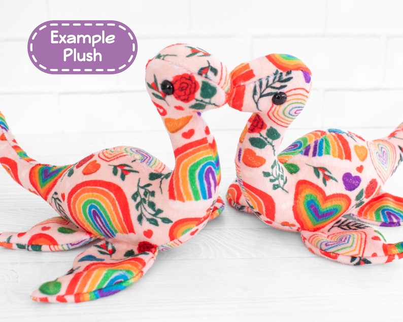 K&ouml;nnte beinhalten: Zwei Pl&uuml;schtierkreaturen mit langen H&auml;lsen und flossenartigen Anh&auml;ngseln. Die Spielzeuge sind mit einem rosa Stoff mit einem Muster aus Regenbogen, Herzen und floralen Elementen bedeckt. Der Text "Example Plush" befindet sich in einem lila Oval.