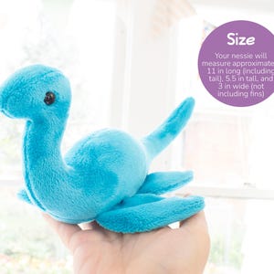 K&ouml;nnte beinhalten: Ein t&uuml;rkisfarbenes Nessie-Pl&uuml;schtier mit langem Hals, kleinen schwarzen Augen und Flossen. Das Spielzeug ist etwa 28 cm lang, 14 cm hoch und 8 cm breit. Der Text "Size" wird in einem lila Kreis angezeigt.