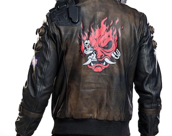 Könnte beinhalten: Eine schwarz-braune Lederjacke mit einer großen rot-weißen Grafik einer stilisierten Dämonenmaske auf dem Rücken. Der Kragen zeigt den Schriftzug SAMURAI in weißen Buchstaben. Die Jacke hat schwarze Schulterdetails und runde Akzente.