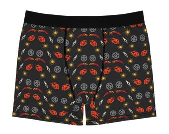 May include: Boxer briefs featuring a black base with a repeating pattern of grey car wheels, white spark plugs, red and orange flames, and yellow starbursts. The garment has a solid black elastic waistband and black stitching along the seams.
