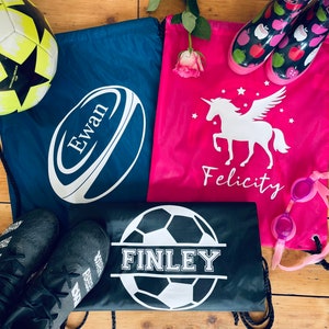 May include: Three drawstring bags with different designs. The first bag is navy blue with a white rugby ball and the name "Ewan" printed on it. The second bag is pink with a white unicorn and the name "Felicity" printed on it. The third bag is black with a white football and the name "Finley" printed on it.