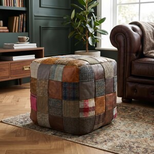 Op de afbeelding: Een vierkante poef opgebouwd uit een patchwork van diverse materialen, waaronder bruine lederen vierkanten en veelkleurige wollen tweed stoffen vierkanten met ruit-, visgraat- en effen patronen in grijze, rode en blauwe tinten.