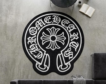 Peut inclure: Un tapis noir circulaire présentant un motif graphique blanc composé d'une croix centrée dans une bordure circulaire. Le texte CHROME HEARTS est imprimé en police gothique blanche le long de la bordure. Le tapis a une forme distincte.