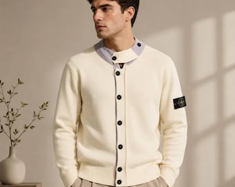 Può includere: Un cardigan in maglia color crema con colletto grigio chiaro, una fila verticale di bottoni scuri sul davanti e una toppa con logo nero e giallo sulla manica sinistra. Il capo presenta maniche lunghe e un orlo a coste in vita.