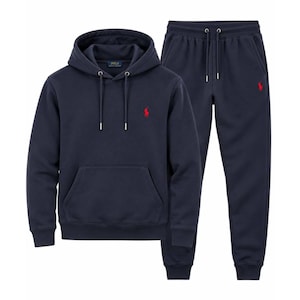 May include: A navy blue hooded sweatshirt and matching sweatpants set. The hoodie features a drawstring hood, a front kangaroo pocket, and a red embroidered Polo Ralph Lauren logo. The sweatpants have an elastic waistband with drawstrings.