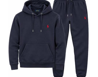 May include: A navy blue hooded sweatshirt and matching sweatpants set. The hoodie features a drawstring hood, a front kangaroo pocket, and a red embroidered Polo Ralph Lauren logo. The sweatpants have an elastic waistband with drawstrings.