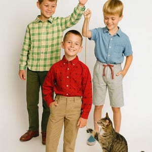 May include: Three young people wearing casual clothing pose with a cat. One wears a red button-down shirt and khaki pants. Another wears a blue shirt and gray shorts. The third wears a green and yellow plaid shirt and green pants.