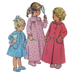 May include: Three girls wearing different nightgowns. The girl on the left is wearing a blue nightgown with white trim and is holding a teddy bear. The girl in the middle is wearing a pink nightgown with a floral print and is holding a hand mirror. The girl on the right is wearing a pink nightgown with white trim.