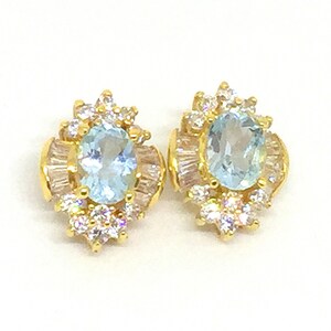 May include: A pair of gold earrings with oval-shaped light blue gemstones surrounded by smaller clear gemstones.