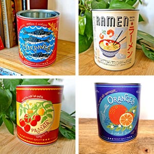 May include: Four decorative tin cans with colorful labels. One features sardines, another ramen, a third passata, and the last oranges. Each can has a silver rim and is designed with vintage-style graphics and text.