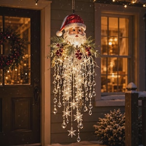 May include: A hanging Santa Claus decoration featuring a red and white hat, a white beard, and green pine branches with red berries. Below the face, numerous illuminated strands hang down, adorned with clear crystal-like teardrops and snowflakes.