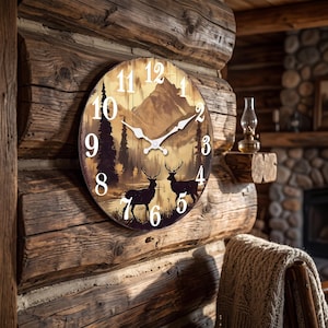 May include: A round wall clock featuring a printed landscape scene of two deer standing near a lake with pine trees and mountains in the background. The clock face has large white Arabic numerals and ornate white metal clock hands.