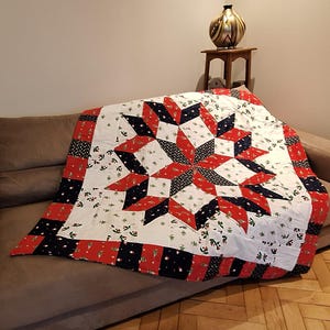 Peut inclure: Une courtepointe avec un grand motif d'étoile centrale en rouge, blanc et bleu marine. Le tissu présente un imprimé répétitif de petits sapins de Noël verts et de baies de houx. La bordure se compose de bandes de tissu rouge et bleu marine.