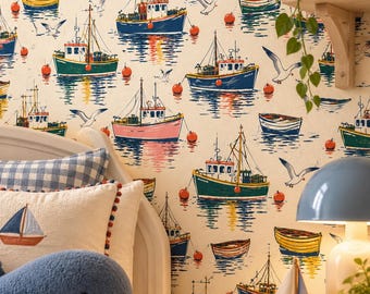 May include: Wallpaper featuring a repeating pattern of colorful fishing boats, small rowboats, and seagulls on a cream background. A blue and white checkered pillow, a plush whale, and a small wooden sailboat model are in the foreground.