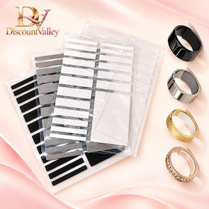 May include: A set of adhesive ring size adjusters in clear plastic packaging, featuring multiple rectangular strips in black, grey, and white. Four rings are displayed to the right: one black, one silver, one gold with a textured finish, and one rose gold with small stones.