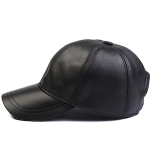 Puede incluir: Una gorra de béisbol negra fabricada con un material liso de acabado mate. La gorra presenta un diseño estructurado de seis paneles con costuras visibles a lo largo de la visera curva y un pequeño botón en la parte superior central.