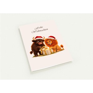 May include: A white greeting card featuring a brown highland cow and an orange lion, both wearing red Santa hats, opening a glowing gift box. The text Frohe Weihnachten is printed in black script above the two animals on the card.