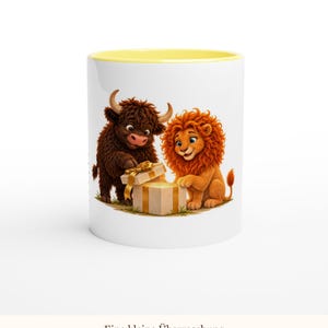 May include: A white ceramic mug with a yellow interior rim featuring a graphic of a brown highland cow and an orange lion opening a beige gift box with a gold ribbon. The text "Eine kleine &Uuml;berraschung" is printed below the illustration.