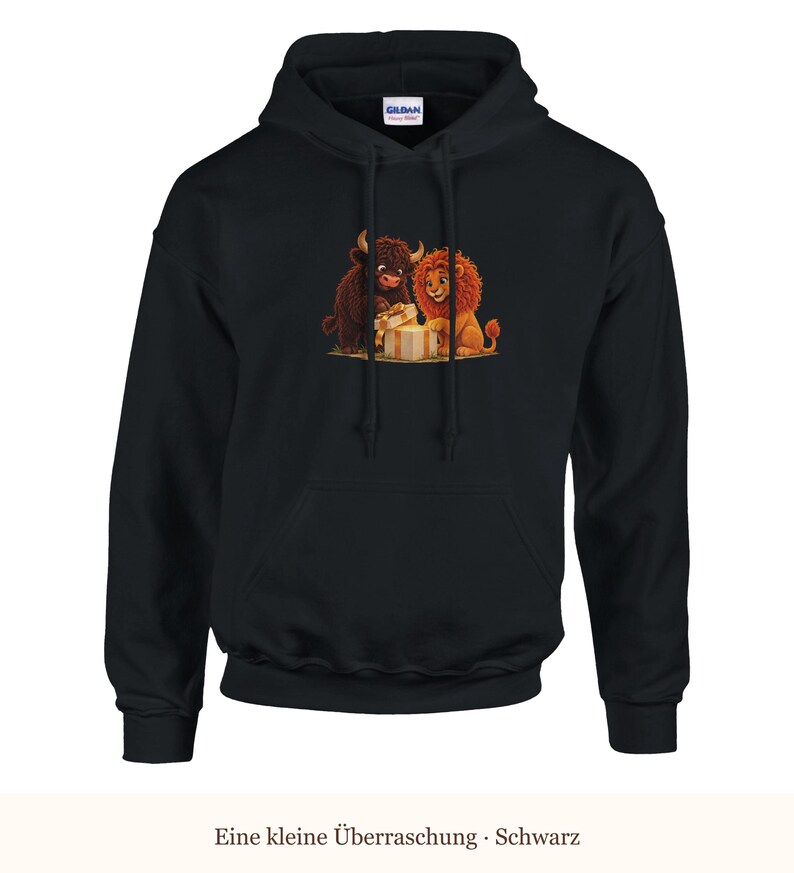K&ouml;nnte beinhalten: Ein schwarzer Kapuzenpullover mit einem Grafikdruck, der ein braunes Hochlandrind und einen L&ouml;wen zeigt, die gemeinsam ein beiges Geschenk mit goldener Schleife &ouml;ffnen. Der Hoodie hat lange &Auml;rmel und eine K&auml;ngurutasche auf der Vorderseite.