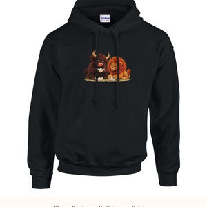 K&ouml;nnte beinhalten: Ein schwarzer Kapuzenpullover mit einem Grafikdruck eines braunen Stiers und eines L&ouml;wen, die zusammensitzen und jeweils ein kleines wei&szlig;es Papierboot halten. Der Hoodie hat lange &Auml;rmel und eine K&auml;ngurutasche auf der Vorderseite.