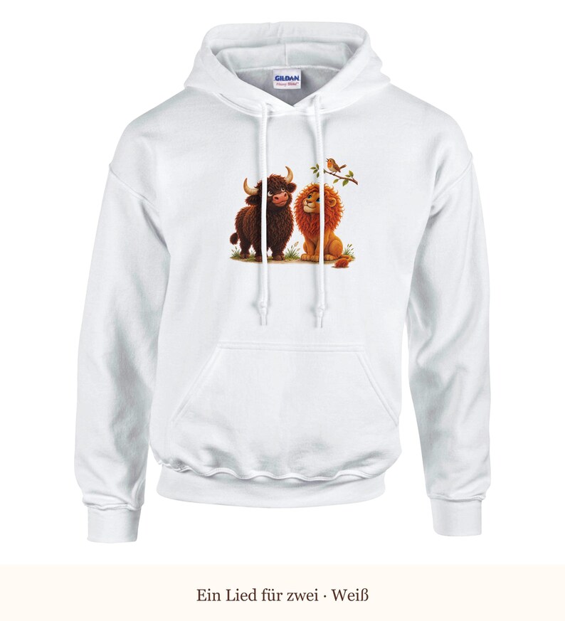 K&ouml;nnte beinhalten: Ein wei&szlig;er Kapuzenpullover mit einem Grafikdruck, der ein braunes Hochlandrind und einen goldenen L&ouml;wen zeigt, die zusammen auf Gras sitzen, mit einem kleinen Vogel auf einem Ast dar&uuml;ber. Der Hoodie hat lange &Auml;rmel und eine K&auml;ngurutasche.