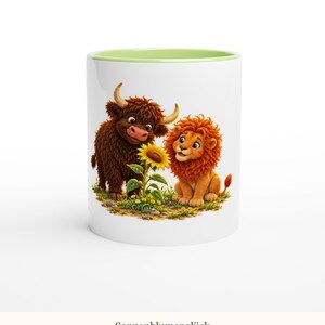 May include: A white ceramic mug with a light green interior rim featuring a colorful illustration of a brown highland cow and an orange lion sitting together next to a yellow sunflower. The text Sonnenblumengl&uuml;ck is printed below.