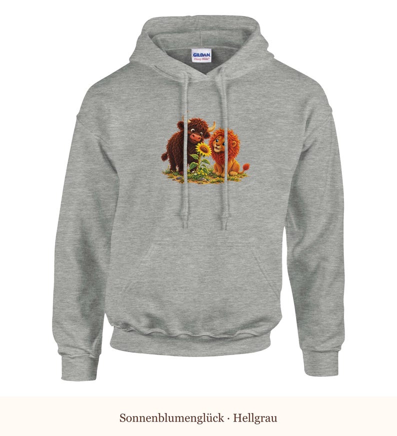K&ouml;nnte beinhalten: Ein hellgrauer Kapuzenpullover mit einem Grafikdruck eines braunen Hochlandrindes und eines L&ouml;wenbabys, die zusammen neben einer gelben Sonnenblume sitzen. Das Kleidungsst&uuml;ck verf&uuml;gt &uuml;ber eine Kapuze mit Kordelzug und eine K&auml;ngurutasche.