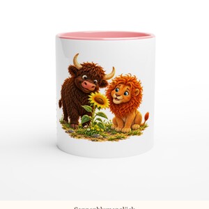 May include: A white ceramic mug with a pink interior and rim, featuring a colorful illustration of a brown highland cow and an orange lion sitting together in a grassy field next to a bright yellow sunflower with the text Sonnenblumengl&uuml;ck.