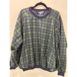 May include: A long-sleeve pullover jacket featuring a green and navy blue plaid pattern. The garment has a dark navy blue ribbed crew neckline, matching navy blue cuffs at the wrists, and a navy blue elasticized hemline at the bottom.