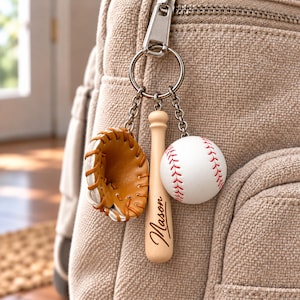 May include: A metal keychain featuring three charms: a miniature tan leather baseball glove with white lacing, a light wood baseball bat engraved with the name Mason, and a white baseball with red stitching, all attached to a silver ring.