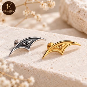 May include: Two ear climbers, one in silver-tone metal with a dark textured inlay and one in gold-tone metal with a matching textured inlay, both featuring a central triangular cutout with a small three-petaled floral motif.
