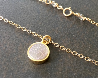 May include: A gold chain necklace with a small, round pendant featuring a white, sparkly stone.