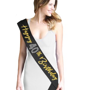 May include: Black satin sash with gold text that reads "Happy 40th Birthday." The number 40 is embellished with rhinestones. The sash is worn diagonally across the body. The sash is a party accessory.