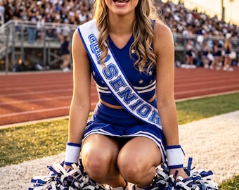 Puede incluir: Un uniforme de animadora azul que consiste en un top corto y una falda con estrellas blancas, junto con muñequeras blancas y pompones azules y blancos. Una banda blanca con el texto azul CHEER SENIOR se lleva sobre el pecho.