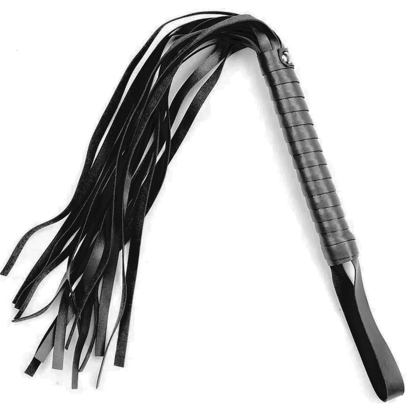 May include: A black leather whip featuring a long, wrapped handle with a secure wrist loop at the base. The top of the handle connects to a series of thin, flexible black leather strips that fan out, creating a long, flowing tail design.