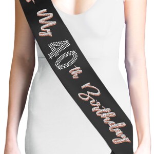 May include: Black satin sash with the text "It's My 40th Birthday" in rose gold glitter and rhinestone accents. The sash is worn diagonally across the body, a celebratory accessory for a milestone birthday.