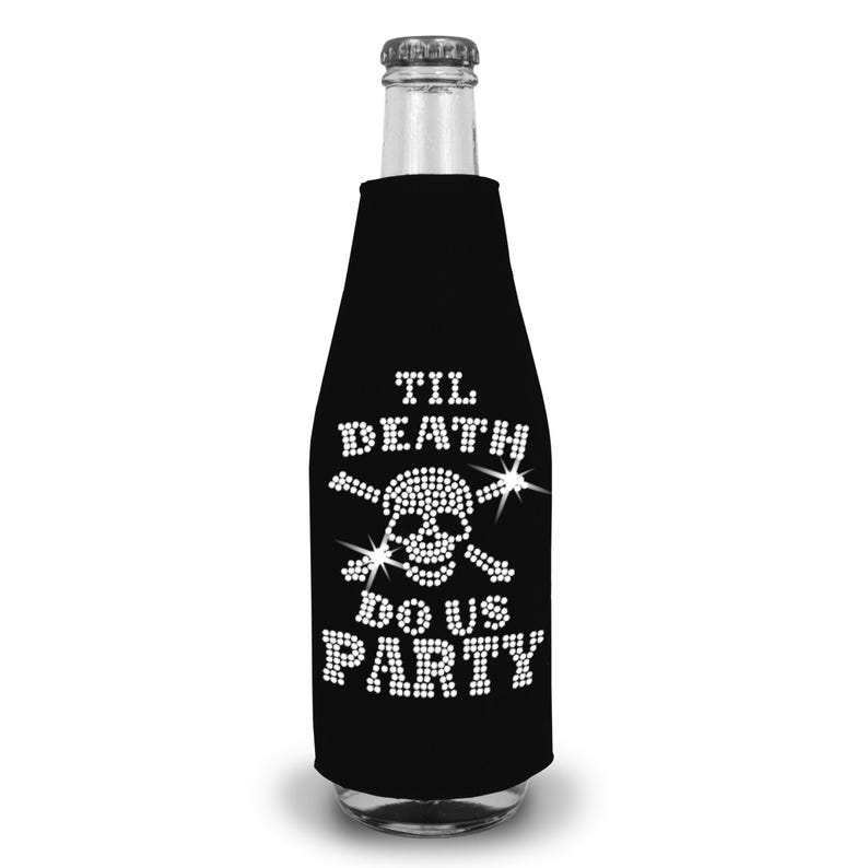 May include: A black bottle sleeve featuring a white rhinestone design of a skull and crossbones. The text "TIL DEATH DO US PARTY" is written in white rhinestones above and below the skull graphic. The sleeve is fitted around a glass bottle.