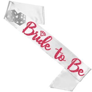 以下が含まれることがあります： 赤いグリッターのスクリプトで「Bride to Be」の文字が入った白いサテンサッシュ。サッシュにはダイヤモンドのグラフィックとハートのシンボルが付いた2つのサイコロが付いています。ブライダルシャワーや独身最後のパーティーに最適なアクセサリーです。