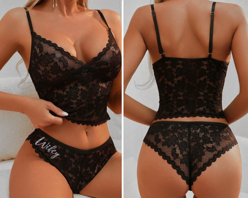 May include: A black lace lingerie set consisting of a camisole with thin adjustable straps and matching knickers. The knickers feature the word Wifey in silver glitter script on the front hip. Both pieces are crafted from floral patterned lace.